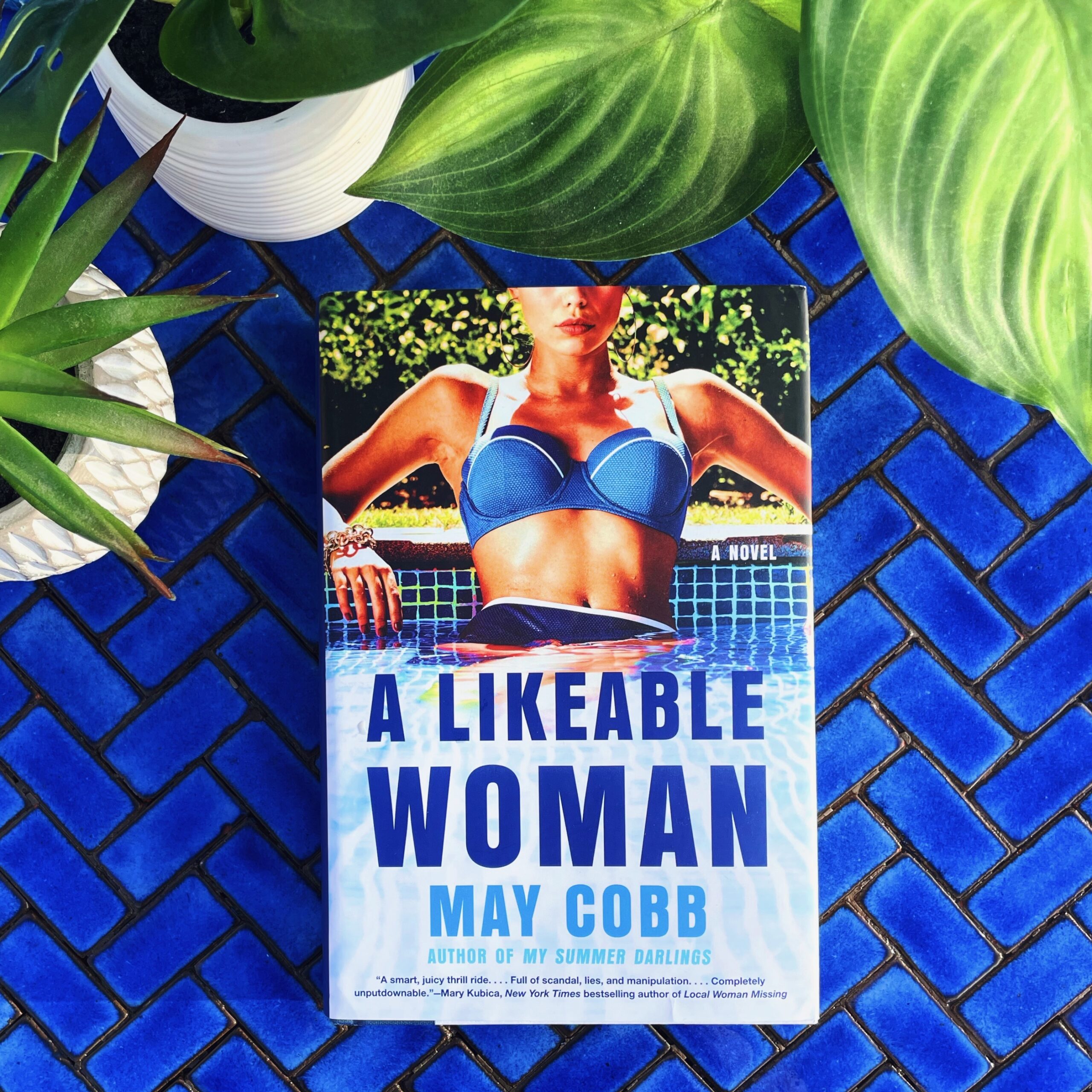 A Likeable Woman is a character-driven psychological thriller by May Cobb featuring a woman in a blue bathing suit on the cover, relaxing in a pool