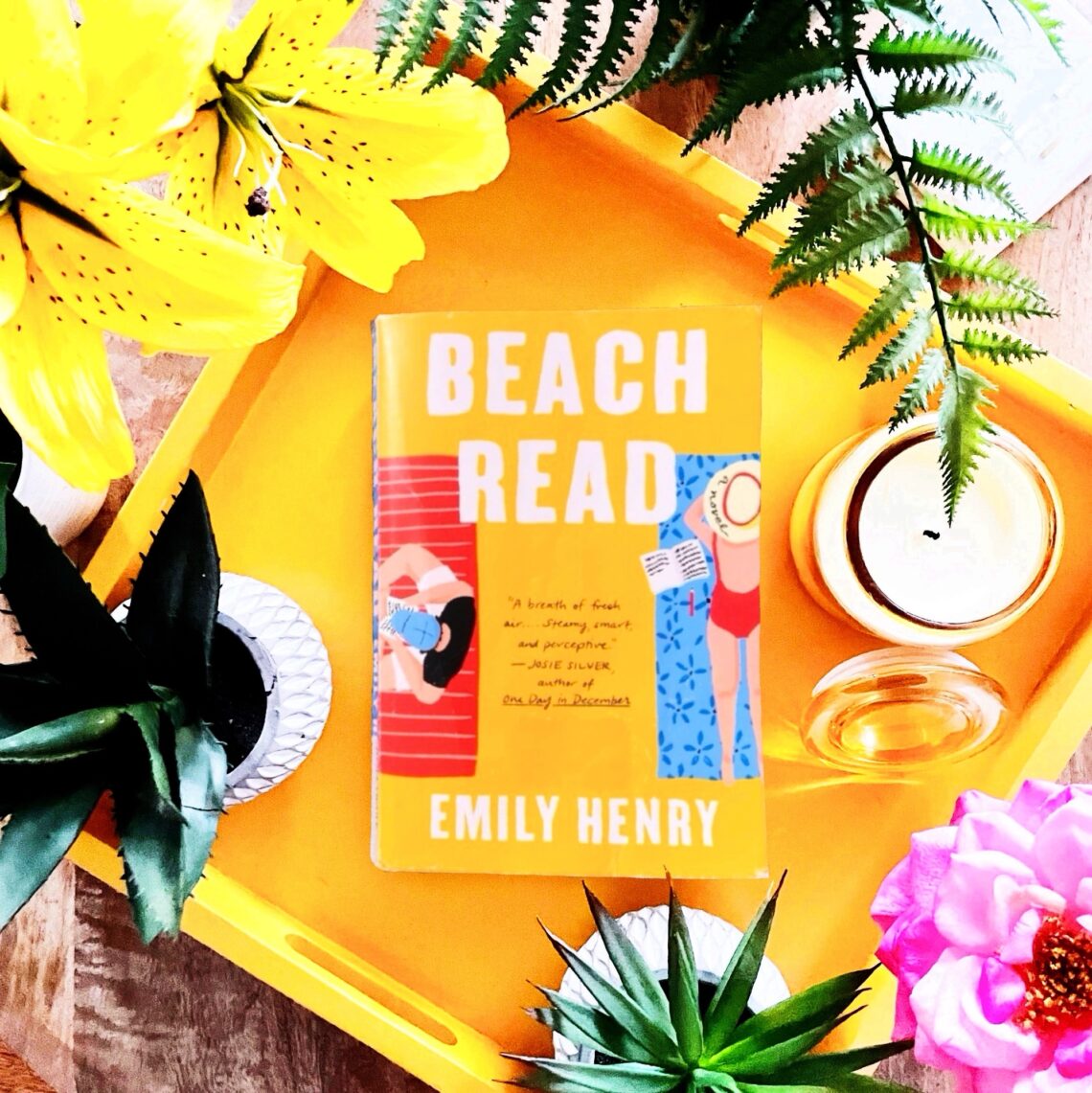 Beach Read is a contemporary fiction book by Emily Henry that features a golden yellow cover with a man and a woman laying on beach towels side by side
